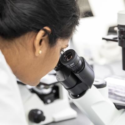 A close-up image of a student intently looking through a microscope in a science lab, focusing on her experiment.